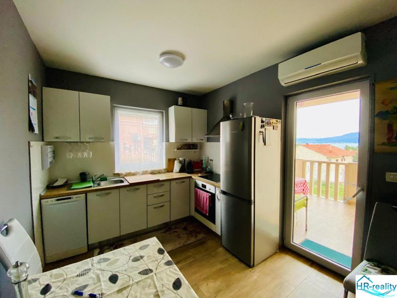 Kuchyně rekreačního apartmánu s podlahou s dřevěným dekorem a světlým nábytkem.