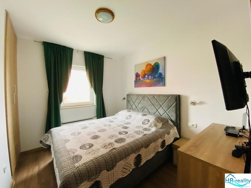 Ložnice v rekreačním apartmánu s pohodlnou postelí, dekorativním obrazem a podlahou s dřevěným dekorem.