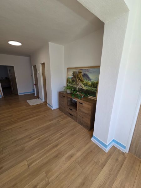 Rodinný dům má podlahu s dřevěným dekorem, komodu a dekorativní obraz na stěně.
