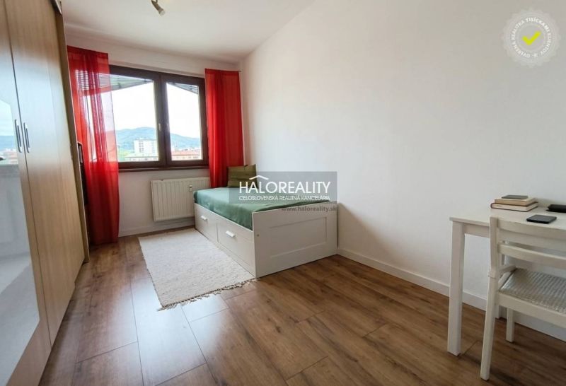 Světlý pokoj s postelí, stolem a podlahou s dřevěným dekorem ve 3-pokojovém bytě.