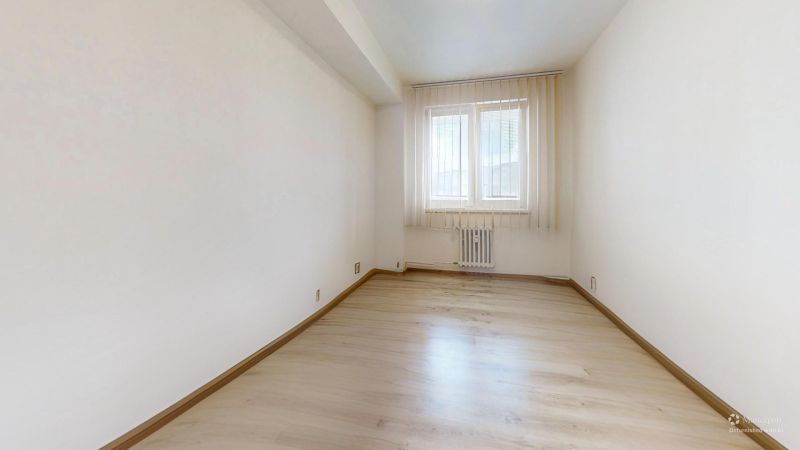 Světlá místnost s oknem a podlahou s dřevěným dekorem v 2-pokojovém bytě.