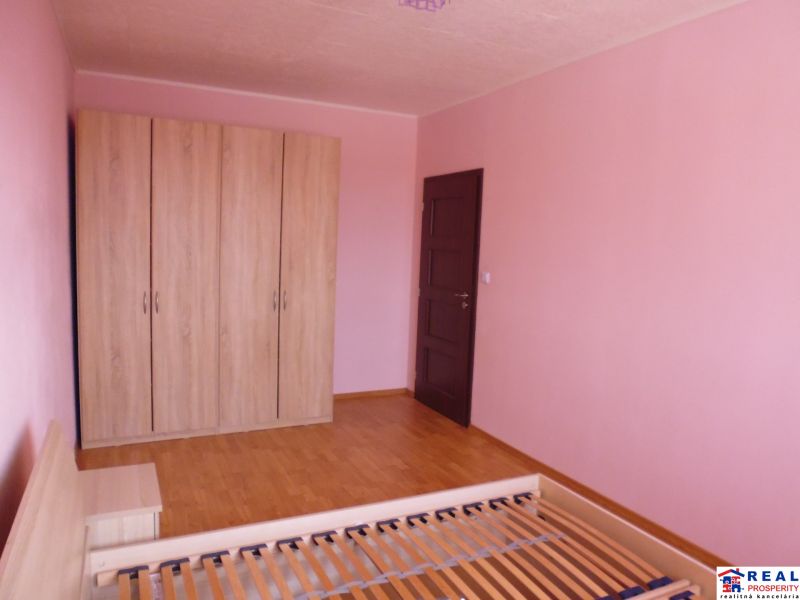 Pokoj v 2-pokojovém bytě s růžovými stěnami, skříní a podlahou s dřevěným dekorem.