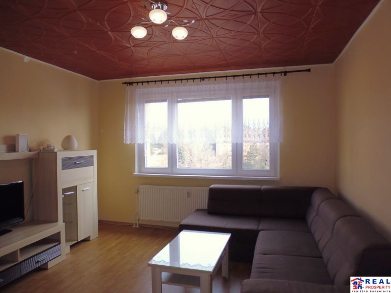 Obývací pokoj v 2pokojovém bytě s hnědým stropem a podlahou s dřevěným dekorem.