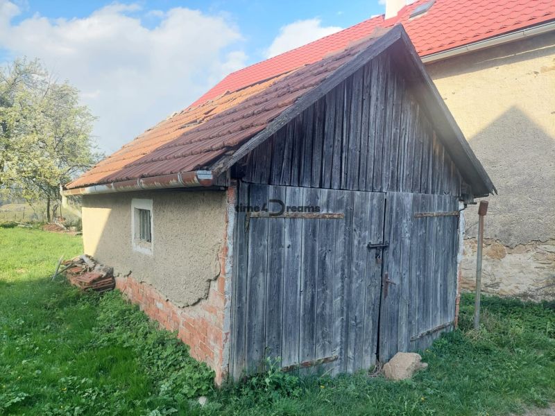 Stará dřevěná garáž na pozemku pro bydlení v Budiné, obklopená zelení a stromy.