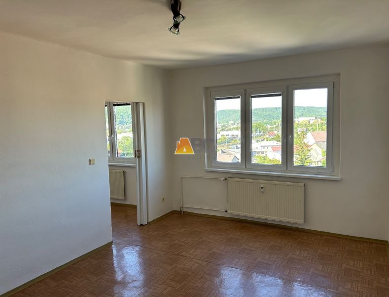 Světlý pokoj se třemi okny a podlahou s dřevěným dekorem v 2pokojovém bytě.
