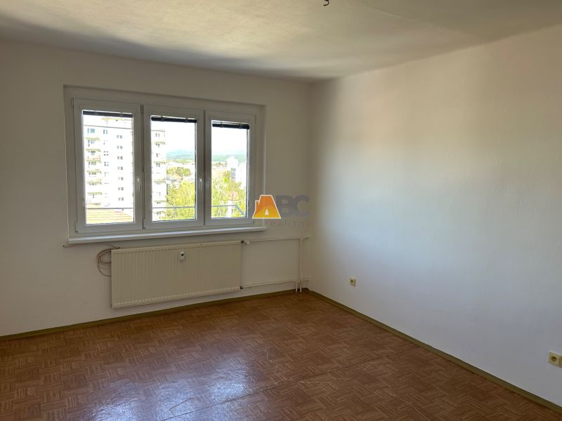 Pokoj 2pokojového bytu s podlahou s dřevěným dekorem a velkým oknem.