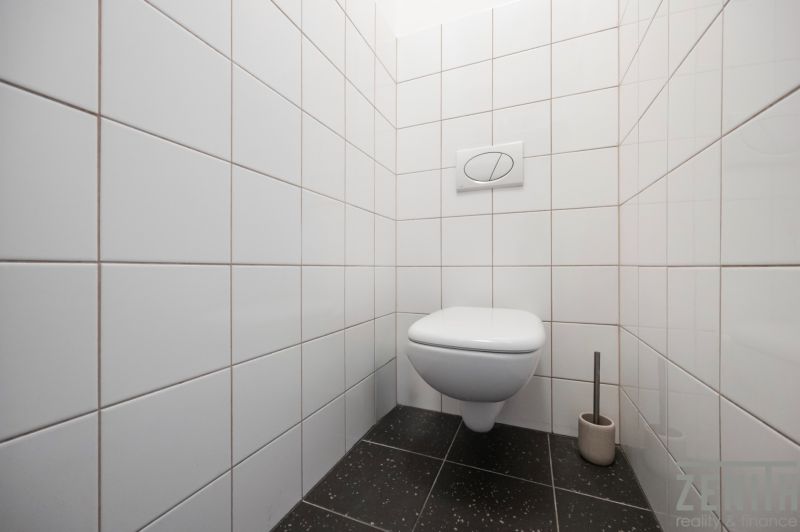 Toaleta s bílými kachličkami a černou podlahou v 2-pokojovém bytě.