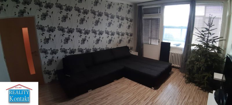 Obývací pokoj v 2-pokojovém bytě s květinovou tapetou a podlahou s dřevěným dekorem.