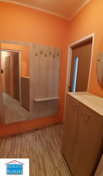 Oranžová předsíň se zrcadlem, věšáky a podlahou s dřevěným dekorem v 2-pokojovém bytě.