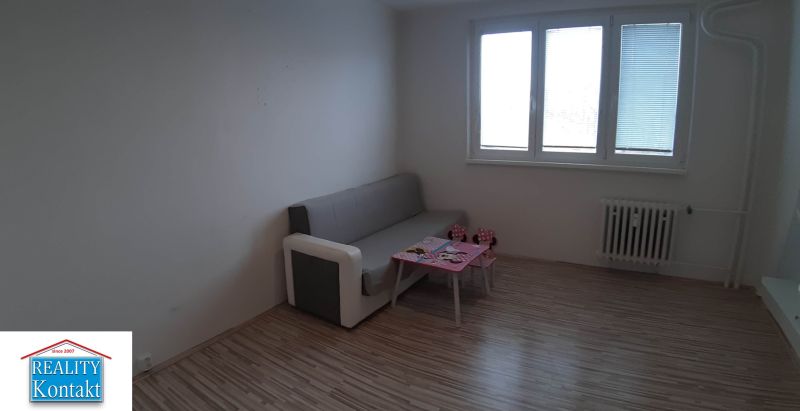 Obývací pokoj v 2pokojovém bytě s pohovkou a stolkem, podlaha s dřevěným dekorem.