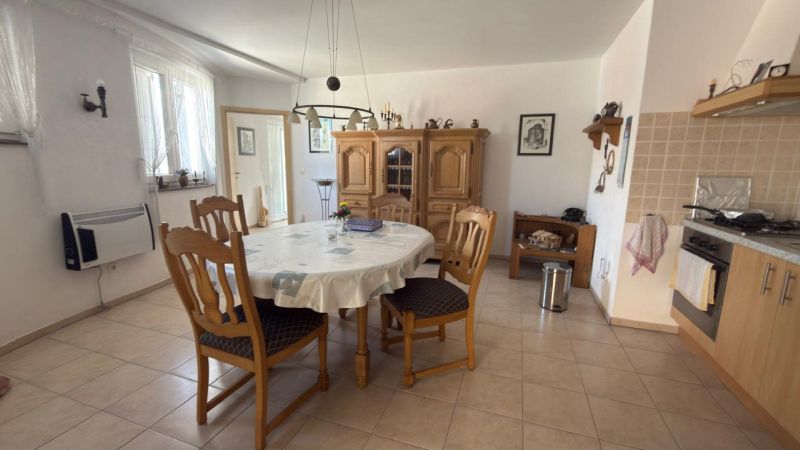 Kuchyně v rodinném domě s kulatým stolem, dřevěnými židlemi a kredencem.