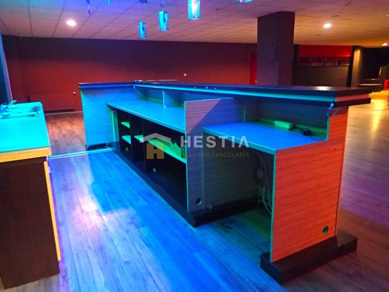 Noční bar s osvětleným pultem, dřevěnou podlahou a prostorem pro obchodní prostory.