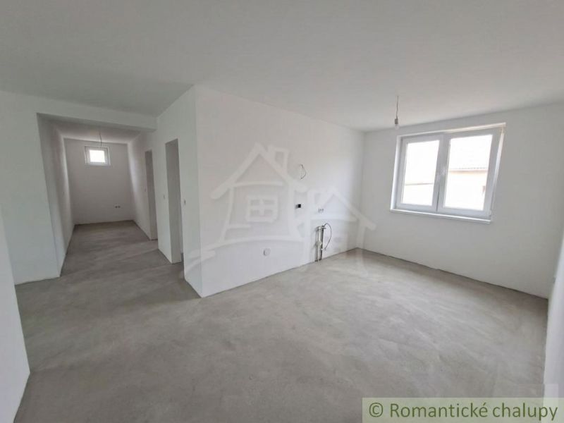 Bílá místnost s oknem, betonová podlaha, vývody na kuchyňskou linku v rodinném domě.