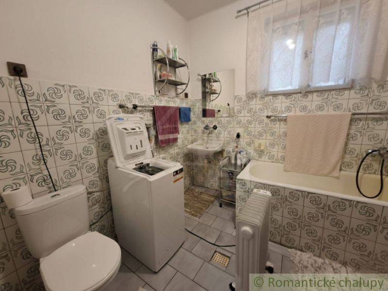 Koupelna v rodinném domě s pračkou, vanou a obklady s květinovým motivem.