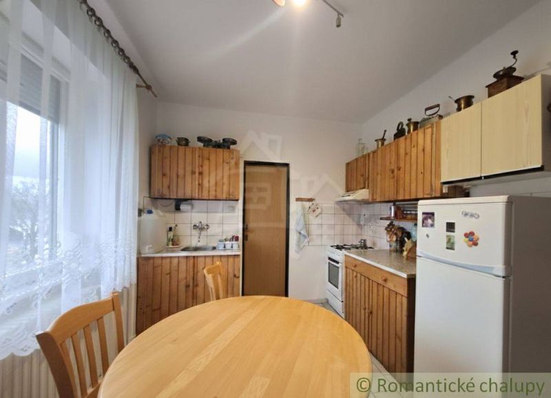 Kuchyně v rodinném domě s dřevěnými skříňkami, jídelní stůl, lednička, židle.