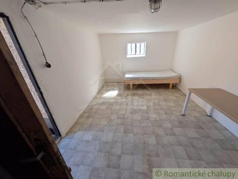 Pokoj v rodinném domě s postelí, stolem a oknem, světlé stěny.