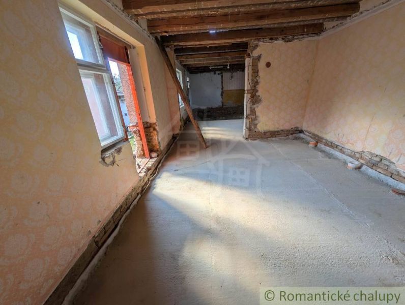 Interiér rodinného domu s odkrytými dřevěnými stropy a poškozenými stěnami.