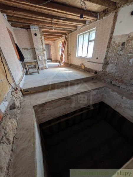 Interiér rodinného domu s odkrytým stropem a surovými stěnami v rekonstrukci.