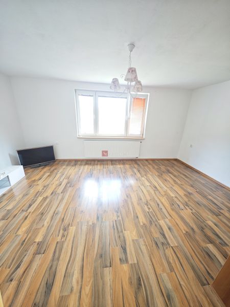 Prostorný obývací pokoj s podlahou s dřevěným dekorem a velkým oknem v 3-pokojovém bytě.