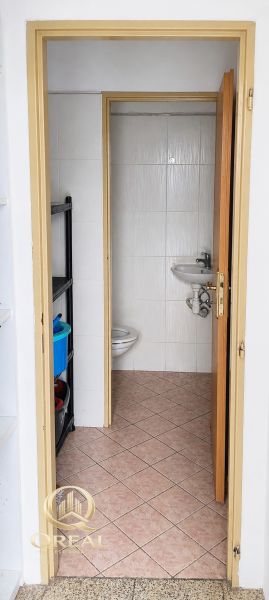 Koupelna v obchodních prostorách s toaletou a umyvadlem, jednoduchý dlaždičkový design.