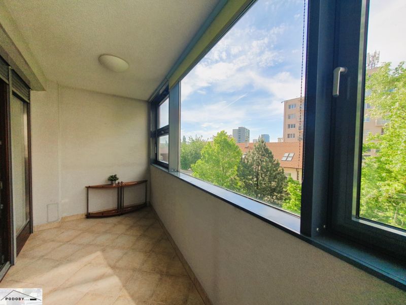 Zasklená lodžie v 3-pokojovém bytě s výhledem na zeleň a městskou panorámu.