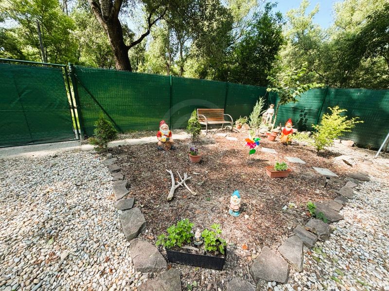 Zahrada s trpaslíky a lavičkou u chaty v Gabčíkovu, obklopená kameny a plotem.