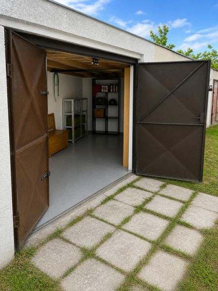 Otevřená garáž na Gúgské ulici v Nových Zámcích s regály a rovným trávníkem.