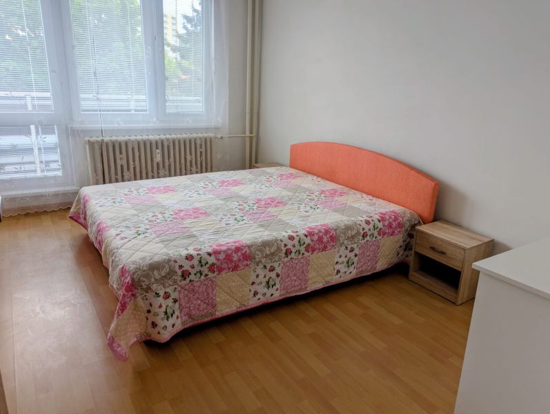 Ložnice s postelí a patchworkovým přehozem ve 2-pokojovém bytě, podlaha s dřevěným dekorem.