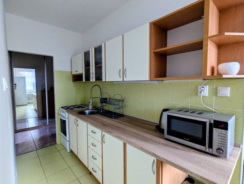 Kuchyně v 2-pokojovém bytě s mikrovlnkou a varnou deskou, směřující do další místnosti.