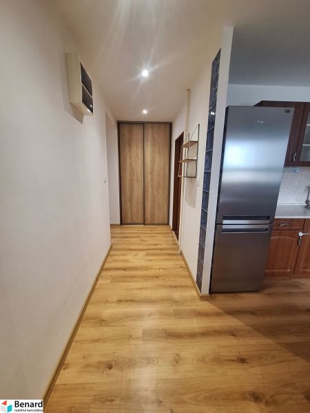 Chodba s vestavěnou skříní a kuchyní v 2pokojovém bytě, dřevěná podlaha, světlé stěny.