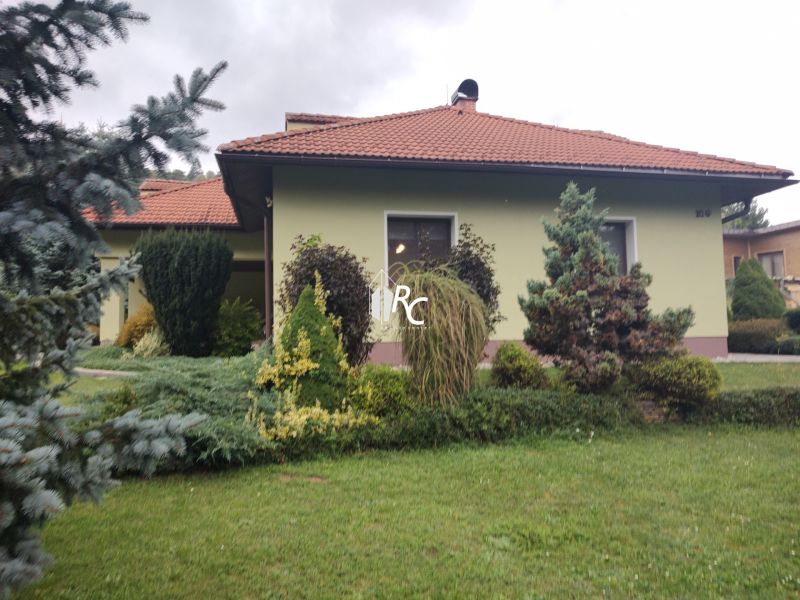 Rodinný dům v Trebostově, vpředu upravená zahrada s rostlinami a stromy.