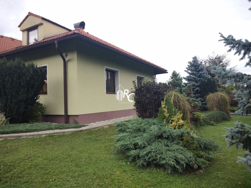 Rodinný dům v Trebostově s upravenou zahradou a dřevěnými detaily střechy.