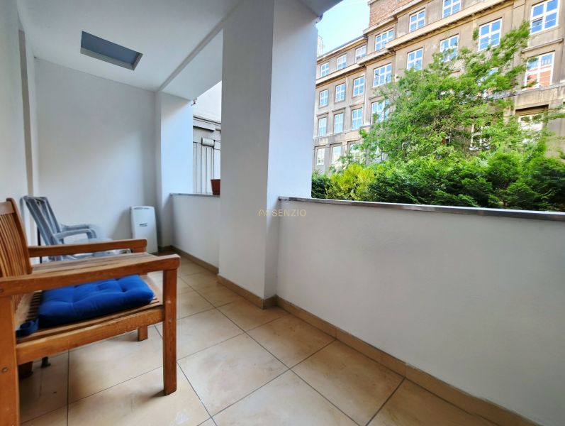 Balkon 2-pokojového bytu s výhledem na zeleň a budovu, posezení s židlemi.