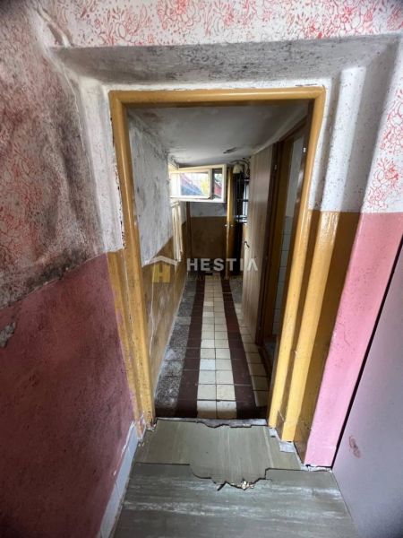Úzká chodba s poškozenými stěnami a dlážděnou podlahou v rodinném domě.