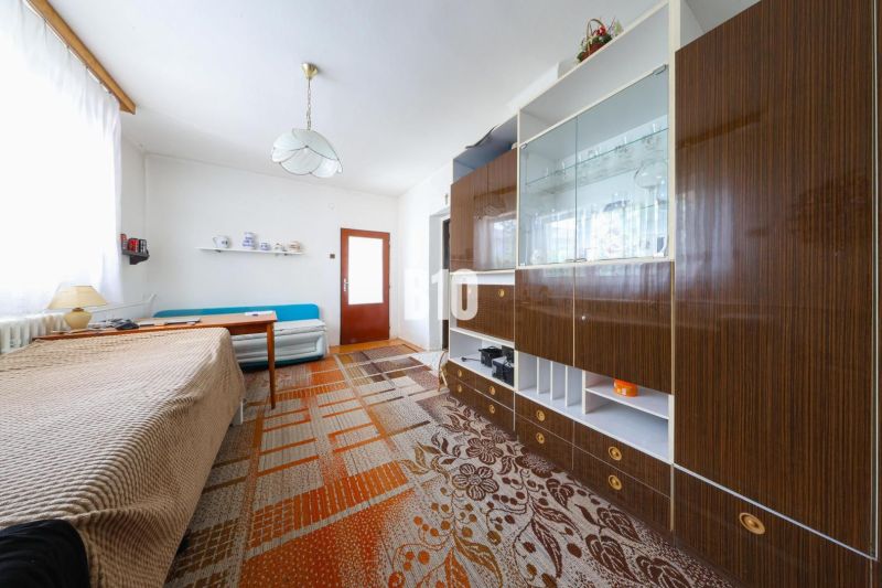 Interiér rodinného domu s pohovkou, skříňkou a jídelním stolem, koberec na podlaze.