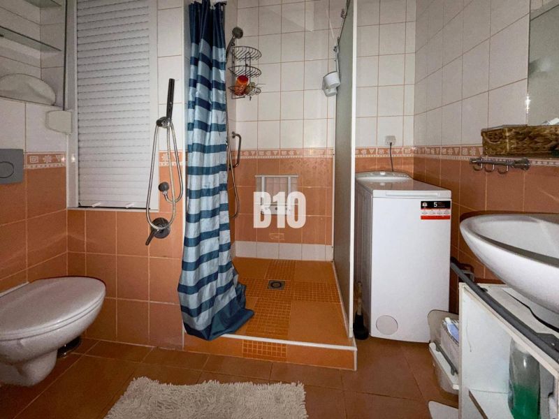 Koupelna v 3-pokojovém bytě s oranžovými obklady, sprchovým koutem, pračkou a WC.