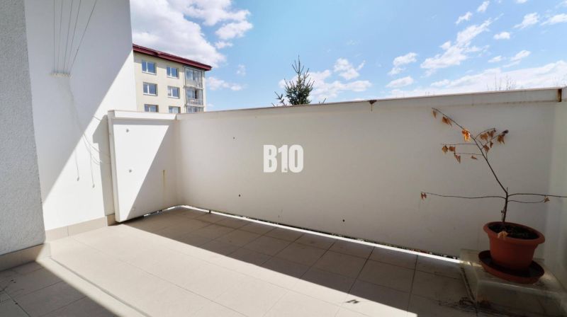 Balkon v 3-pokojovém bytě. Rostlina v květináči, dlažba, částečný výhled na sousední budovu.