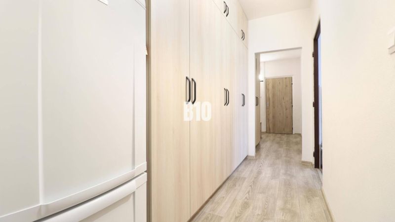 Chodba v 3-pokojovém bytě s podlahou s dřevěným dekorem a světlými skříněmi.