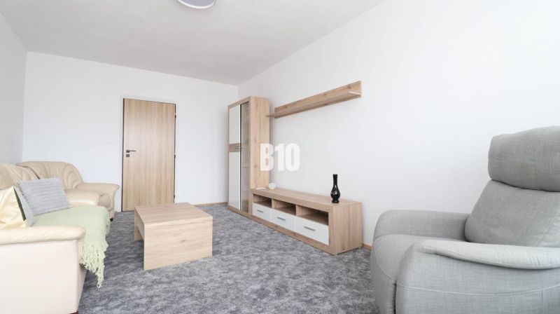 Obývací pokoj s béžovou sedačkou, šedým křeslem a nábytkem s dřevěným dekorem ve 3-pokojovém bytě.