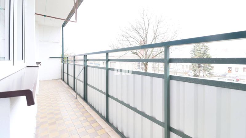 Balkon 3pokojového bytu s výhledem na stromy a dlažbou.