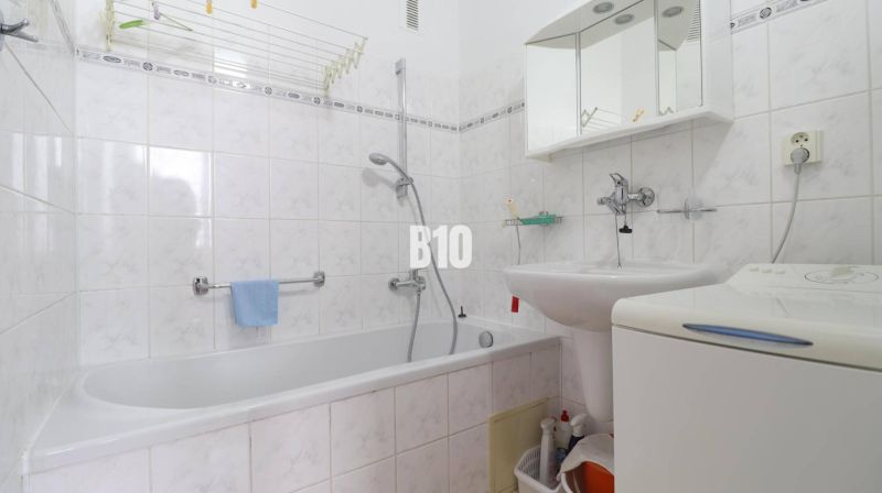 Koupelna ve 3-pokojovém bytě s vanou, umyvadlem, zrcadlem a pračkou.