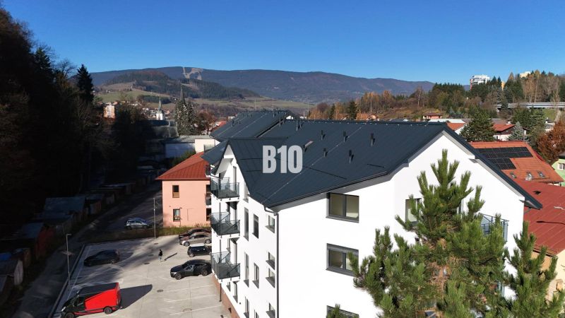 Novostavba bytového domu v Dolním Kubíně, s výhledem na hory a parkovištěm.