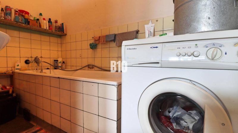 Koupelna v rodinném domě s vanou, pračkou a čisticími prostředky na poličce.