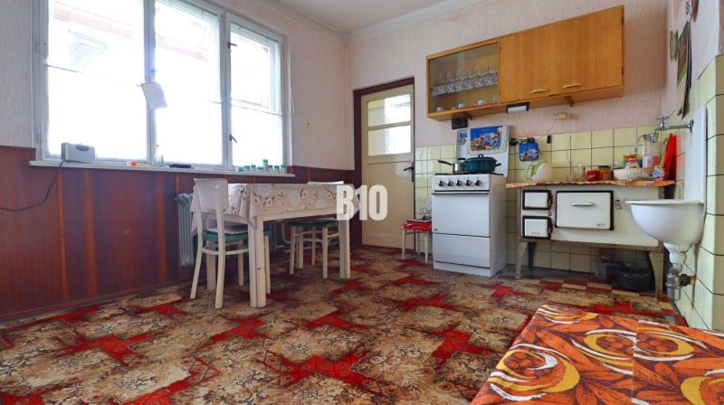Kuchyně v rodinném domě s retro nábytkem, kamny a výrazným kobercem.