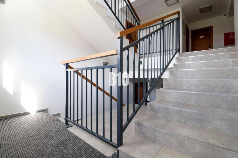 Schodiště s kovovým zábradlím v Rekreačním apartmánu, světlo proniká oknem.