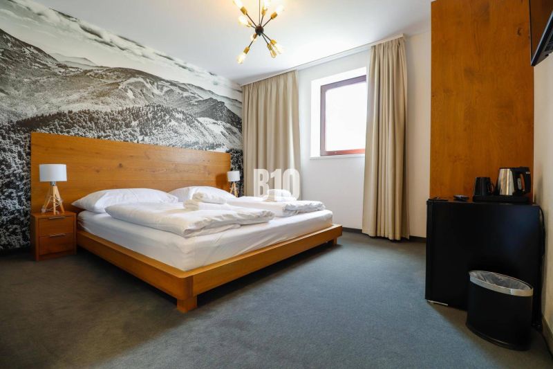 Ložnice v rekreačním apartmánu s dřevěnou postelí a velkoformátovou fotografií krajiny.