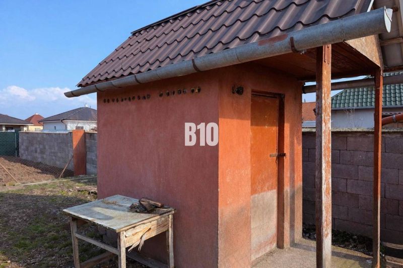 Malá zděná stavba u rodinného domu v Levicích, s plechovou střechou a dřevěným stolem.