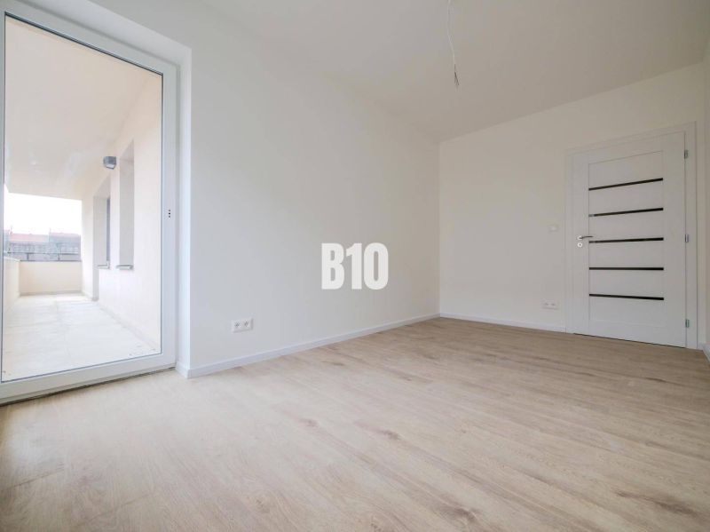 Pokoj s podlahou s dřevěným dekorem a velkými dveřmi na balkon v 3pokojovém bytě.