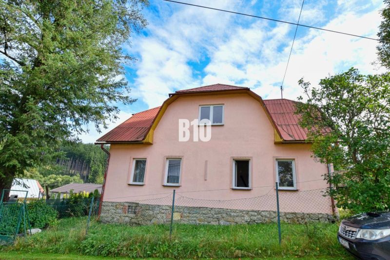 Rodinný dům v Makově s kamenným základem a červenou střechou obklopený zelení.