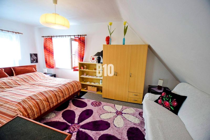Útulná ložnice v chatě s pestrobarevným kobercem, skříňkou a manželskou postelí.
